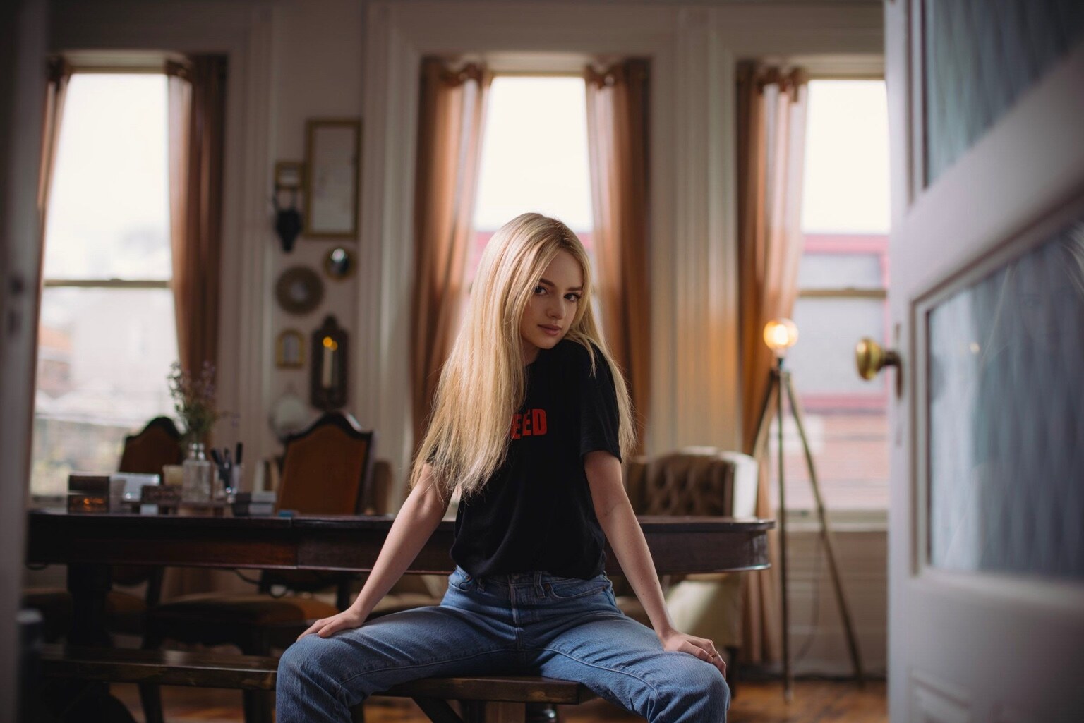 Madison Campbell seated on a bench in a sunlit room wearing a black T-shirt and jeans